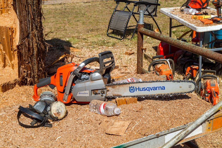 A Husqvarna chainsaw with ear protectors and sawdust in an outdoor forestry setting.