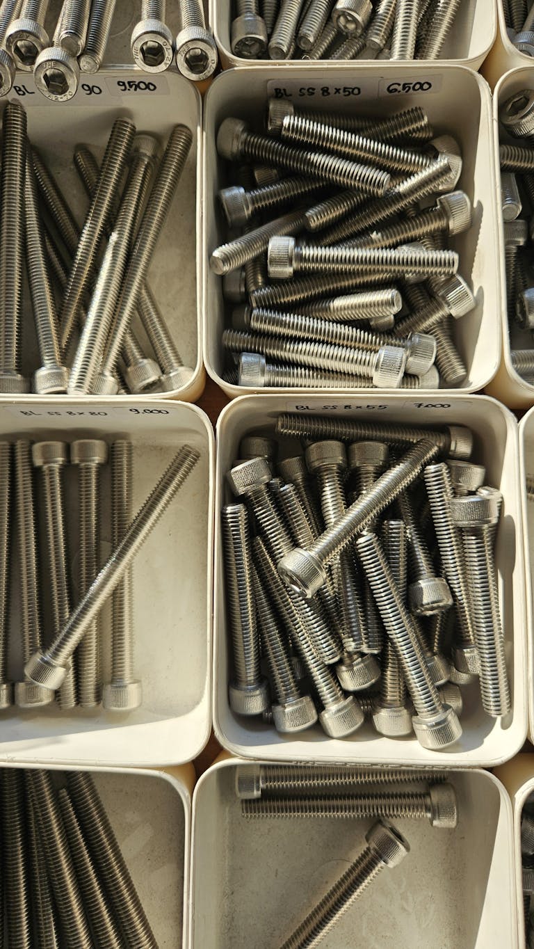 Close-up of various metal bolts stored in organized white bins.