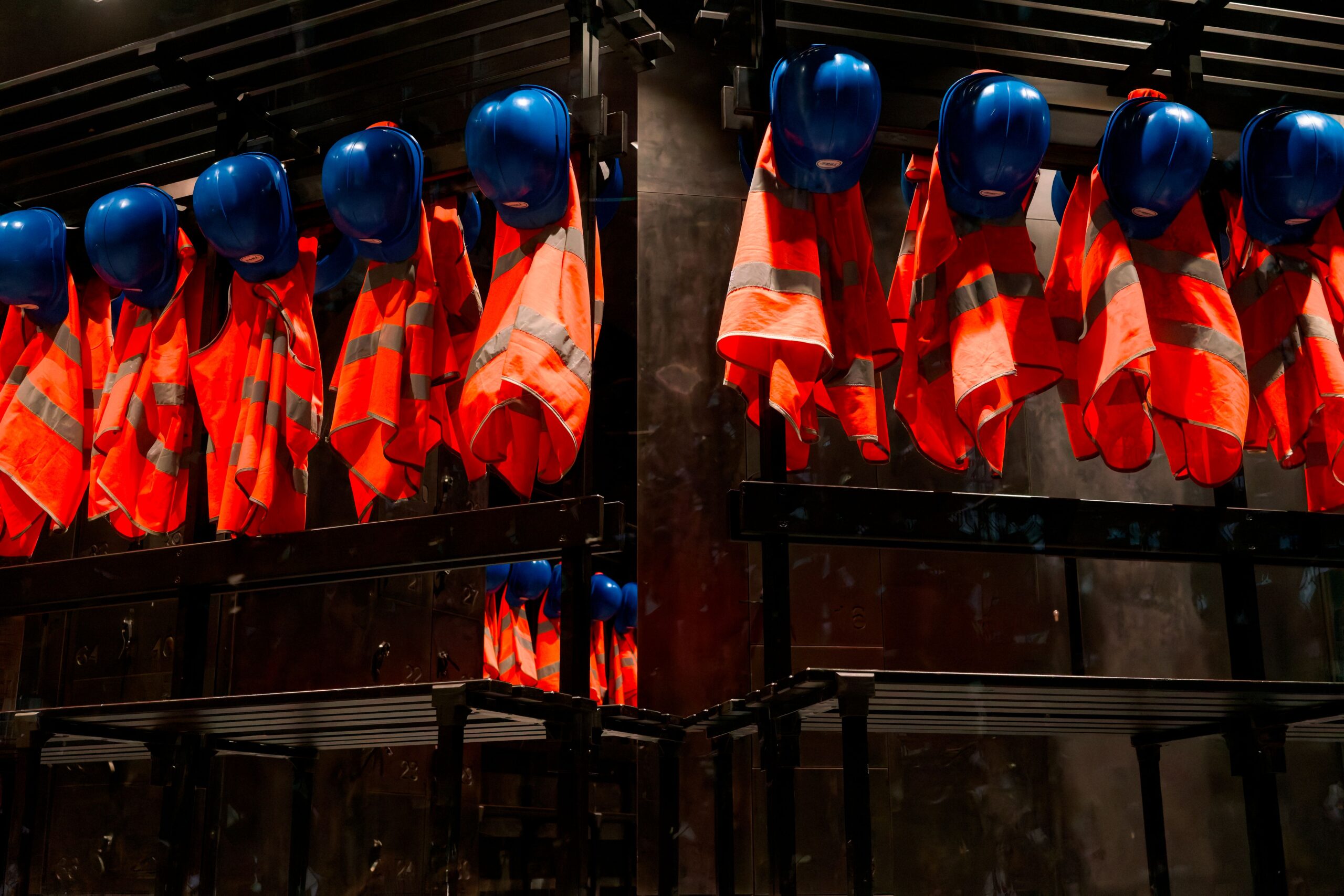 Row of orange safety vests and blue helmets hanging in industrial setting